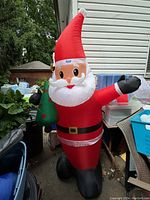 Front view of the large inflatable Santa Claus standing outdoors, showing red suit, white beard, black boots, and holding a small green Christmas tree.