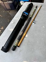 Pool cue fully disassembled into two parts along with black carrying case displayed on a table outdoors.