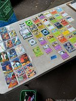 Several Pokémon cards laid out neatly on a table in plastic protective sleeves, showing characters, Pokémon creatures, and energy cards.