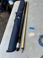 Photo showing two pieces of a pool cue apart and a black soft case with branding laying flat on a table.