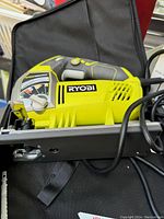 Ryobi jigsaw close-up showing handle, vent, brand logo, and metal baseplate.