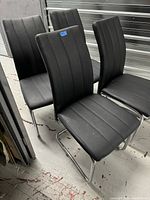 Set of four black modern chairs arranged on a concrete floor, showing shape, upholstery, and cantilever chrome base design.