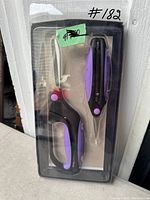 Front view of original packaged scissors set with two scissors, purple and black handle, safety lock visible