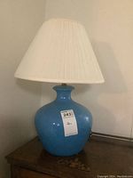 Full view of vintage blue ceramic base lamp with white shade on wooden surface showing height and overall condition.