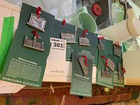 Photo of the full set of ten pewter souvenirs representing historic Kingston buildings, mounted on green backing cards with red loops for hanging.