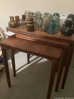 Front view of three teak nesting tables nested together with decorative glass insulators on top