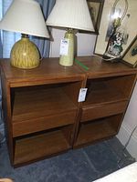 Two wood nightstands side by side on carpeted floor with lamps and decor items on top