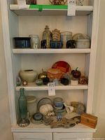 Full view of three white shelves with assorted pottery, carvings, souvenirs including elephants, sand dollars, and bottles.