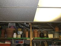 Shelf with various terracotta planters, pots, ceramic pots, baskets and gardening supplies stored in basement under ceiling tiles