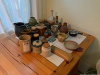 Wide shot of the entire assortment on wooden table near window, showing pitchers, crocks, jars, and decorative pieces.