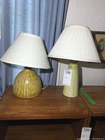 Photo showing two pottery lamps side by side on wooden furniture, featuring their overall size and shape.