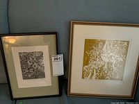 Two framed prints leaning against a couch showing one black and white and one green and white mushroom woodcut prints.