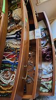 Three wooden drawers open showing collections of jewelry and scarves
