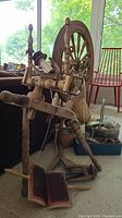 Side angle showing entire antique wooden spinning wheel and baskets with wool and supplies on the floor.