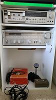 Two-tier shelf showing top Hitachi C-818 cassette deck with manual, below Hitachi SR-704 receiver and bottom shelf holding AKG headphone box, Discwasher box and microphone stand