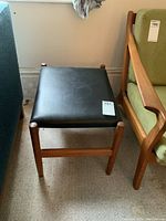 Top-front view of stool showing black vinyl seat and teak frame