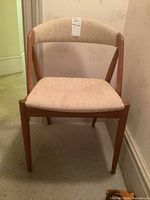 Front view of teak armless dining chair showing beige fabric upholstered seat and backrest.
