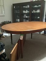 Full view of oval table with one leaf leaning against a leg