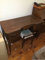Overall view of vintage wooden vanity with matching bench on wooden floor. Vanity has four drawers and shows some surface wear.