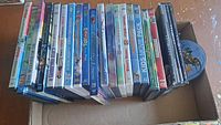 Photo showing 23 DVDs neatly arranged inside a box, titles visible including animated and family movie titles.