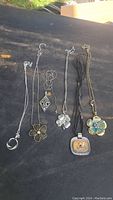Six vintage necklaces with floral and decorative pendants displayed on dark surface
