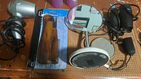 Photo showing two small handheld hair dryers, pack of amber plastic combs in packaging, standing makeup mirror, and small handheld mirror on wooden surface.
