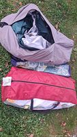 Purple camping tent bag with tent fabric and parts visible inside, lying on grass.