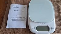 Digital kitchen scale with instruction manual showing brand and product details.