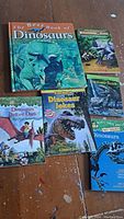 Photo showing all six dinosaur books fanned out, titles visible for most books including 'The Best Book of Dinosaurs', 'Dinosaur Before Dark', and 'KidsWorld Dinosaur Jokes'.