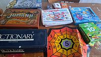 Lot of colorful board games and games boxes arranged on a surface: Jumanji, Spirograph, Lost Cities, Guess 10, Dictionary First Edition, among others.