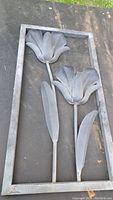 Full view of the rectangular metal framed garden art showing two stylized flowers with stems and leaves inside the frame.