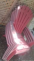 Stacked red plastic Adirondack chairs showing side and front profiles.