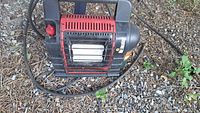 Front view showing red and black Mr. Heater propane heater with metal grille and attached hose.