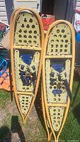 Two pairs of wooden framed snowshoes with tan decking and blue bindings, angled view outdoors on grass.