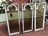 Three Gothic-style sash windows with white wooden frames and caramel textured art glass standing outdoors on a brick surface.