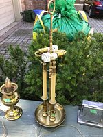 Photo of a polished brass lamp base showing multiple vertical columns, round base plate, bulb socket with pull-chain switch and finial, sitting on outdoor surface.