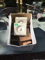 Box on table contains approximately 15 Victorian interior corner blocks for casing trim, some white painted, some natural wood, with decorative circular design.