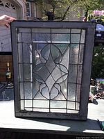 Rectangular decorative crystal glass window with leaded metal design laid on a surface outdoors with visible wear and rust on the frame.