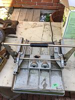 Dry mounting press with metal base, crank handle, and heat plates on a table.