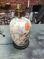 Full view of the ceramic lamp base showing the floral pattern and brass lamp fitting mounted on a wooden base.