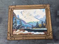 Full view of the framed vintage oil painting showing the mountains, trees, and water.