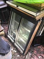 Ten vintage wooden window sashes stacked upright with visible wavy glass panes, showing wood frames and signs of age.