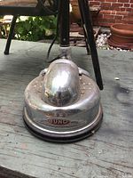 Close-up photo of the chrome-polished floor polisher head showing the Juno badge and art deco styling.