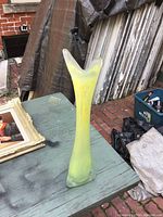 Tall glass vase with flared Y-shaped top and yellow-green interior color on outdoor wooden surface