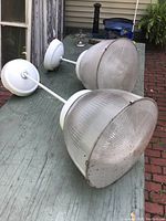 Two large plastic pendant light fixtures with ribbed translucent globes and white mounting bases and stems, displayed on an outdoor table.