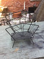 Oblique front-side view of the black metal wire magazine rack showing angled sides and perforated base.