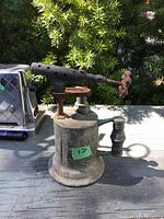 Single photo of a vintage plumbers torch, showing cylindrical metal tank, burner nozzle with holes, knobs, and handle, set outdoors.