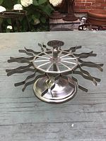 Side view of vintage metal rubber stamp holder showing circular base, center knob, and 20 wavy clip arms