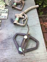 Photo showing two metal hose nozzles with trigger handles and one black metal rotary sprinkler on a weathered wooden table outdoors.