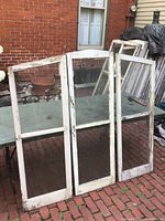 Three rectangular vintage wooden window panels with glass, showing wear and white paint chipping.